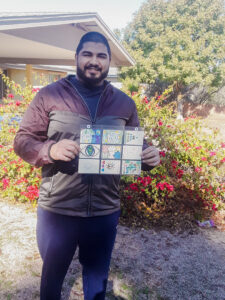 A smiling dark skinned man stands holding a sleeve of 9 samples of artwork created in this project.