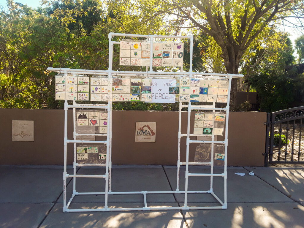 A freestanding structure located in a park with artwork hanging from it.