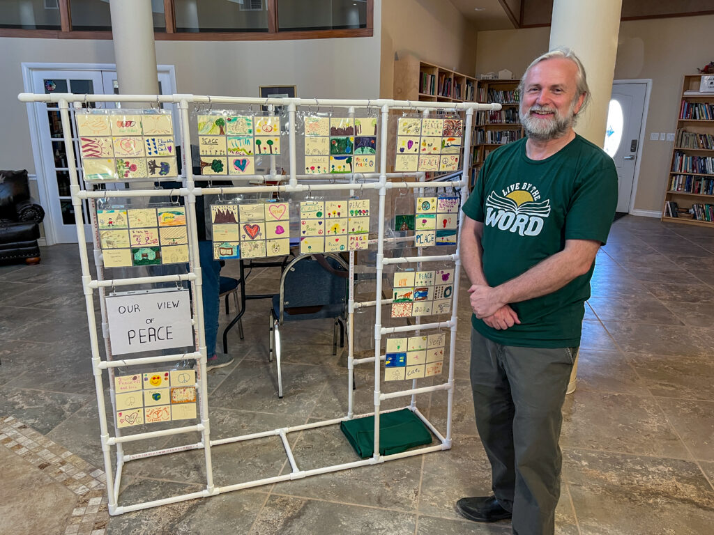 A man standing next to a a construction of pvc pipe with drawings hanging from it.