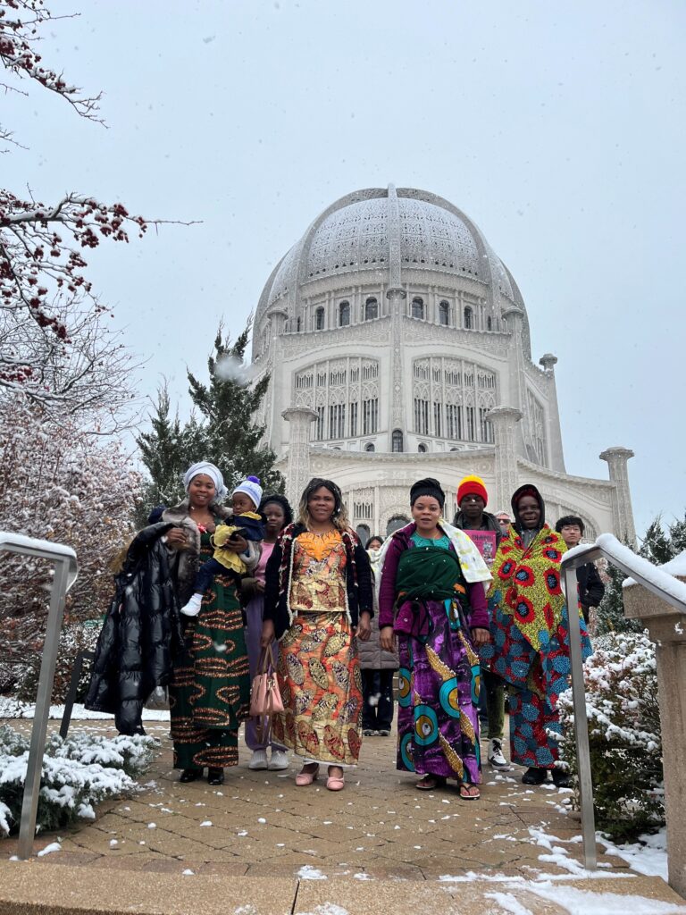 Congolese Bahá'ís in brightly colored clothing gather on the steps of the House of Worship as snow flakes swirl around them.