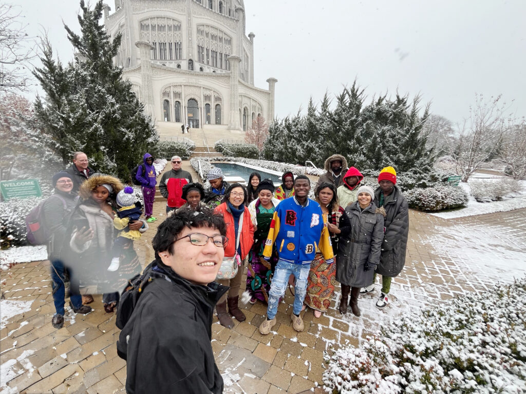 Congolese Bahá'ís in brightly colored clothing gather on the steps of the House of Worship as snow flakes swirl around them.