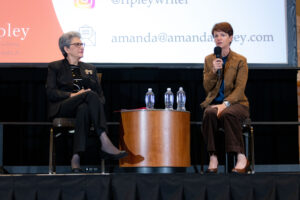 The author of "High Conflict" presents on stage with microphone as Hoda Mahmoudi listens.