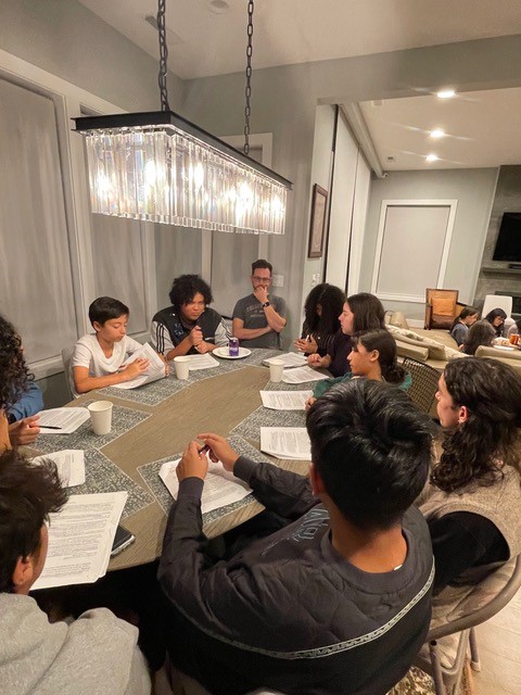 Candid group portrait of Washington youth during a deepening on Bahá'í elections gather around under a modern chandelier at a dining room table.
