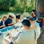 Group painting at a table surrounded by trees