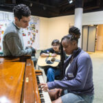 A young girl the piano while others listen